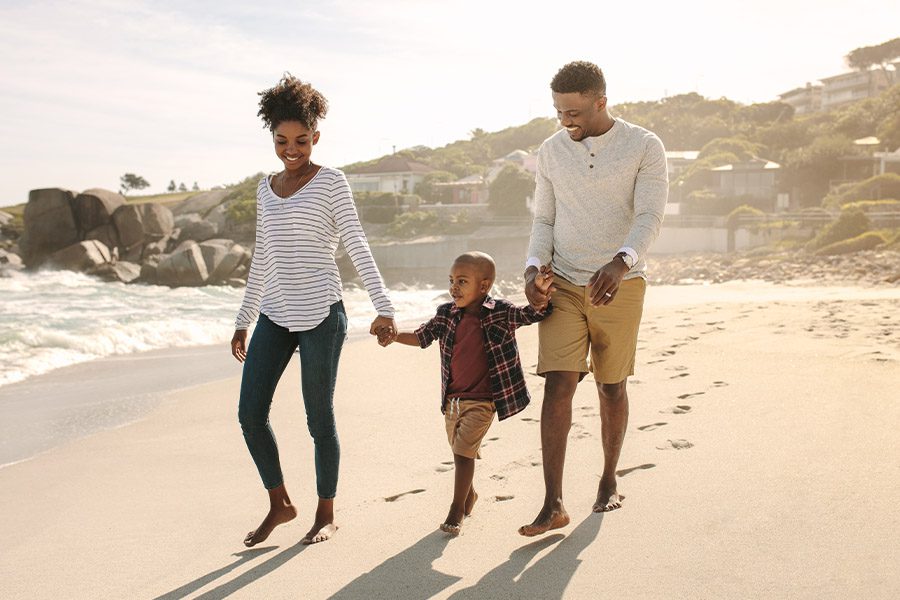 About Our Agency - Happy Family With Young Son Walking Along the Beach at Dusk