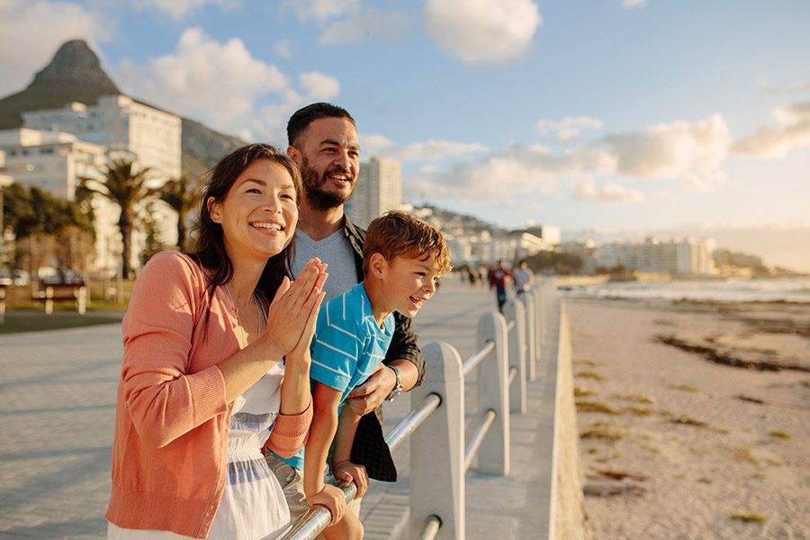 Contact - Young Family Having Fun on a Day Out Near the Sea With Tall Buildings and Coast in the Distance